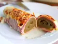 Endive au jambon gratinée, enroulée et coupée en deux, servie sur une assiette blanche avec une sauce crémeuse.