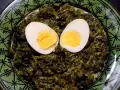 Un plat d'épinards à la crème, parsemé de deux moitiés d'œufs durs, sur une assiette verte décorée.