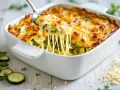Une cuillère soulève un gratin de courgettes fondant, le fromage filant promet un délice.