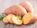 Patates douces entières et tranchées, prêtes à cuire. Une touche de persil frais pour la décoration.