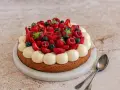 Un délicieux gâteau aux fraises, garni de framboises, myrtilles et crème vanillée. Parfait pour une occasion spéciale.