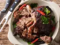 Gigot d'agneau au four cuisson lente, effiloché, garni de piments rouges et de persil frais. Un délice à partager.