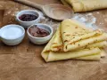 Crêpes dorées empilées, accompagnées de confiture, de pâte à tartiner au chocolat et de sucre. Un délice pour le petit-déjeuner ou le goûter.