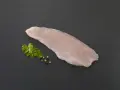 Une escalope de dinde crue, prête à être cuisinée, accompagnée de persil frais et de grains de poivre sur fond sombre.