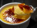 Une cuillère prélève un morceau de crème brûlée, révélant sa texture onctueuse sous une croûte de caramel craquante.