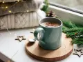 Une tasse de chocolat chaud fumant, entourée de décorations de Noël et de lumières scintillantes, promet un moment de réconfort.