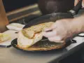 Une main retourne une crêpe dorée dans une poêle fumante. Sur le côté, du beurre frais attend. Ces meilleures crêpes promettent un délice.