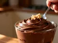 Une cuillère plonge dans une délicieuse mousse au chocolat au lait, garnie de miettes dorées.