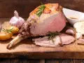 Gigot d'agneau rôti, parfait pour une recette d'agneau pascal. Accompagné de pommes de terre, ail et romarin sur une planche en bois.