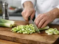 Préparation d'une recette poireaux : un chef coupe des poireaux en dés sur une planche en bois.
