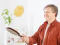 Un homme souriant s'amuse à retourner une crêpe en plein vol avec une poêle.