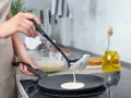 Une louche verse de la pâte à crêpes dans une poêle. On dirait qu'il y a trop de beurre dans la pâte à crêpes, elle est très liquide !