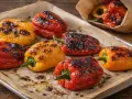 Poivrons rouges, jaunes et oranges grillés au four, sur une plaque recouverte de papier cuisson. Les marques de grill sont bien visibles.