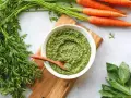 Un bol de pesto de fanes de carottes, avec des carottes fraîches et du basilic à côté.