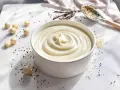 Un bol de ganache vanille onctueuse, parsemé de grains de poivre et de quelques billes de chocolat blanc. Des gousses de vanille et une cuillère de graines complètent la scène.