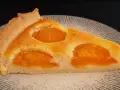 Une part de tarte aux abricots dorée, avec des fruits juteux incrustés dans une pâte moelleuse, sur une assiette texturée.