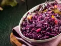 Un plat de chou rouge recette, cuisiné avec des épices et des morceaux de pomme, servi dans un bol blanc.