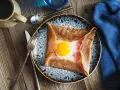 Une galette de sarrasin garnie d'un œuf au plat et de jambon, un des nombreux types de crêpes salées. Servi sur une assiette avec des couverts.