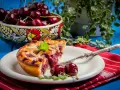 Une part de tarte aux cerises, garnie de menthe fraîche, sur une assiette blanche avec une fourchette. Un bol de cerises est visible en arrière-plan.