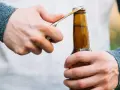 Main gauche tenant une bouteille, main droite utilisant un objet pour ouvrir la bouteille sans tire bouchon.