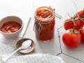Un pot de coulis de tomates maison, des tomates fraîches et une cuillère de sel, prêts pour une recette savoureuse.