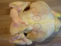 Un poulet cru sur une planche à découper en bois. Deux cercles noirs entourent des zones de chair où l'on voit des fibres musculaires. On dirait que le sot l'y laisse.