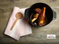 Souris d'agneau à la cocotte en fonte, tendres et savoureuses, prêtes à être dégustées. Une cuillère en bois et une serviette rose complètent la scène.