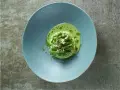 Délicieuse cuisson petit pois frais, servis dans une assiette bleue avec une émulsion verte et des éclats d'amandes.