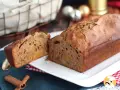 Un délicieux pain d'épices aux fruits confits, coupé en deux, sur une assiette blanche. Des bâtons de cannelle et des décorations de Noël en arrière-plan.