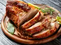 Un rôti de porc au four, coupé en tranches, sur une planche en bois. Le temps cuisson rôti de porc au four moelleux est parfait pour ce plat savoureux.