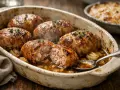 Six savoureuses crepinettes de porc dorées, servies dans un plat en terre cuite avec des oignons caramélisés et une sauce savoureuse.