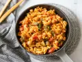 Un plat de cuisson orzo savoureux avec des pois chiches, des poivrons rouges et des épinards dans une sauce tomate.