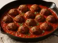 Boulettes de bœuf haché mijotant dans une sauce tomate savoureuse, garnies de persil frais. Une recette réconfortante.