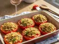 Six tomates provençales garnies d'une chapelure croustillante et d'herbes, dans un plat à gratin. Un verre de rosé et des couverts sont à proximité.