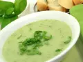 Un bol de soupe à l'oseille crémeuse, garnie d'herbes fraîches, avec du pain en arrière-plan.