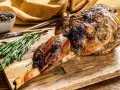 Gigot d'agneau rôti, doré et savoureux, garni de romarin et de moutarde, prêt à être dégusté.