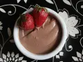 Délicieuse crème au chocolat onctueuse, garnie de deux fraises fraîches, servie dans un bol blanc sur une assiette noire décorée.