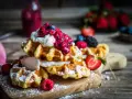 Pile de gaufres traditionnelles garnies de crème fouettée et de fruits rouges, saupoudrées de sucre glace. Un délice pour une recette de gaufre traditionnelle réussie.