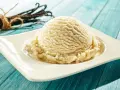 Une boule de glace maison à la vanille, servie sur une assiette blanche, avec des gousses de vanille en arrière-plan.