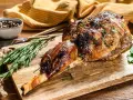 Selle d'agneau rôtie, garnie de romarin et de moutarde, sur une planche en bois avec des herbes fraîches.