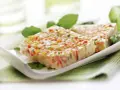 Tranches de terrine de légumes colorée, garnie de feuilles vertes, sur une assiette blanche.