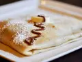 Crêpe pliée, saupoudrée de sucre glace, décorée de chocolat fondu et d'une rondelle de banane. La meilleure recette de pâte à crêpes pour un délice !
