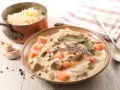Un plat de blanquette de veau crémeuse avec des carottes, des champignons et des herbes, servi avec du riz dans une casserole en cuivre.