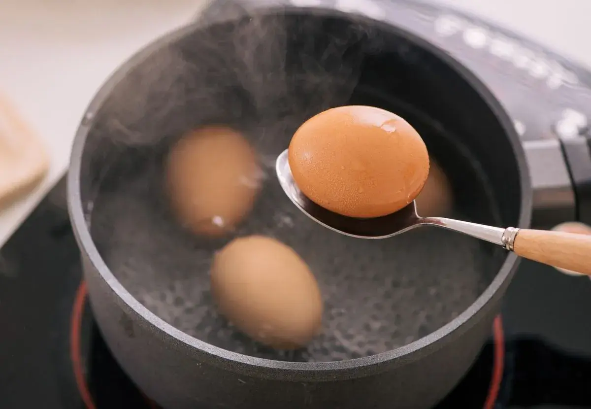 Un œuf mollet est retiré d'une casserole d'eau bouillante à l'aide d'une cuillère. La vapeur s'élève des œufs dans la casserole.