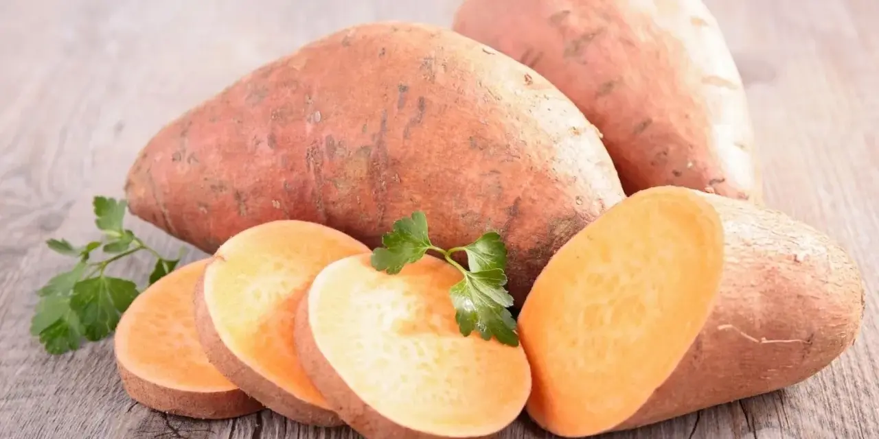 Patates douces entières et tranchées, prêtes à cuire. Une touche de persil frais pour la décoration.