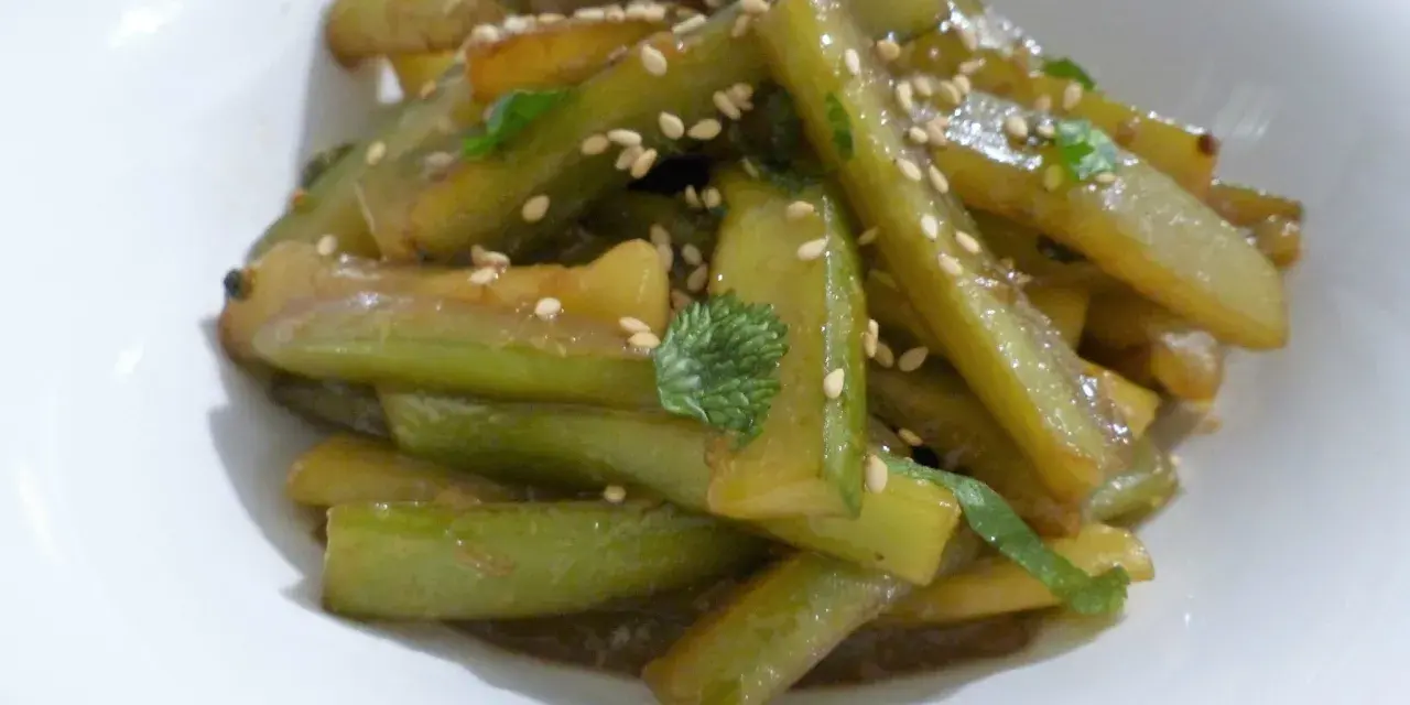 Délicieuse recette concombre cuit, garnie de graines de sésame et de persil frais, servie dans un bol blanc.