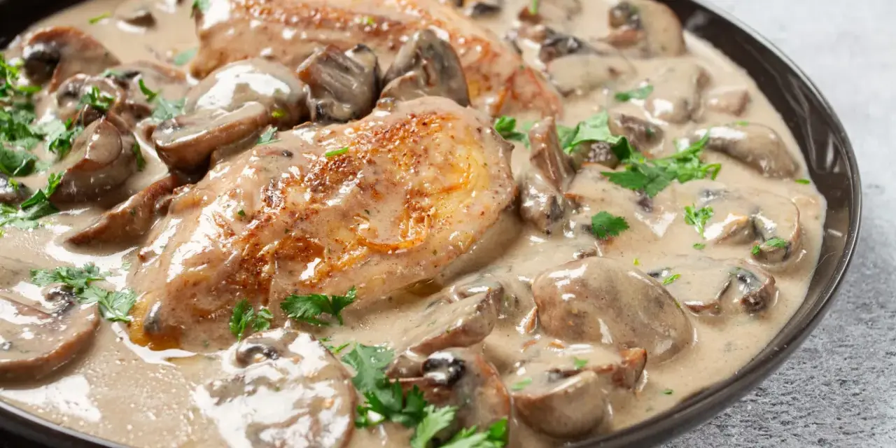Un plat de poulet à la crème onctueuse, parsemé de champignons et de persil frais. Un délice crémeux qui invite à la dégustation.