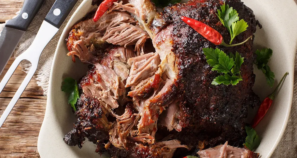 Gigot d'agneau au four cuisson lente, effiloché, garni de piments rouges et de persil frais. Un délice à partager.