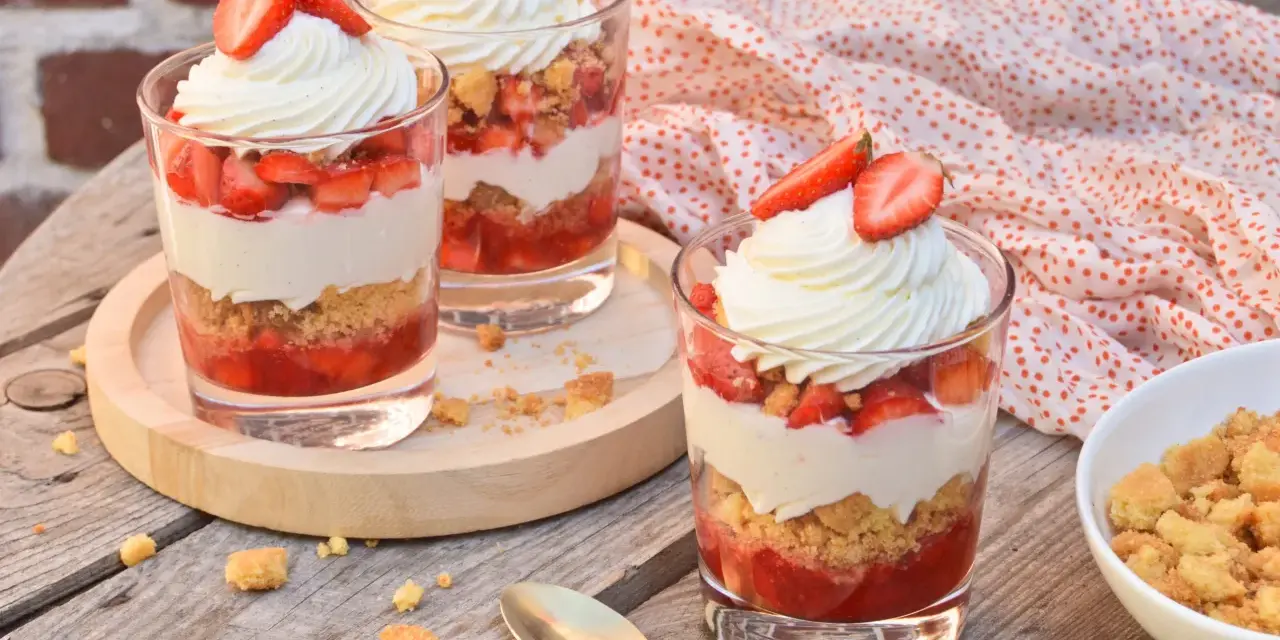 Trois verrines fraise mascarpone, garnies de crème fouettée et de fraises fraîches, sur une table en bois.