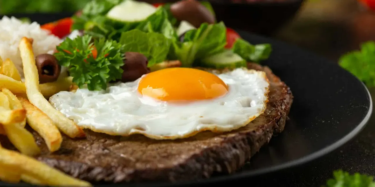 Un plat de steak a cheval savoureux avec un œuf au plat, des frites dorées, du riz blanc et une salade fraîche.
